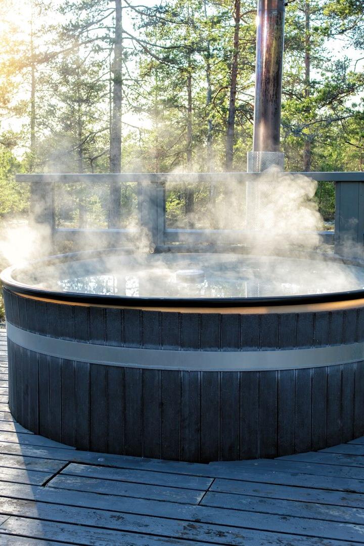 Ein dampfender Whirlpool steht auf einer Holzterrasse im Wald bei Sonnenschein.