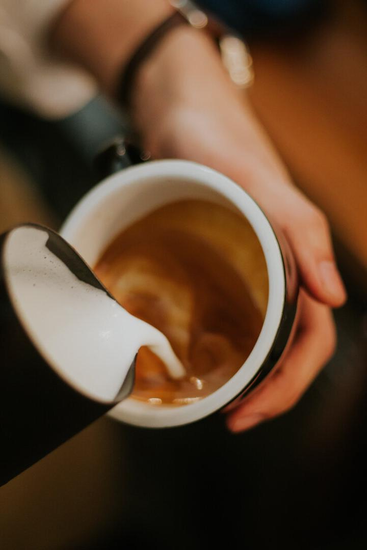 Jemand gießt Milch in eine Tasse Kaffee.