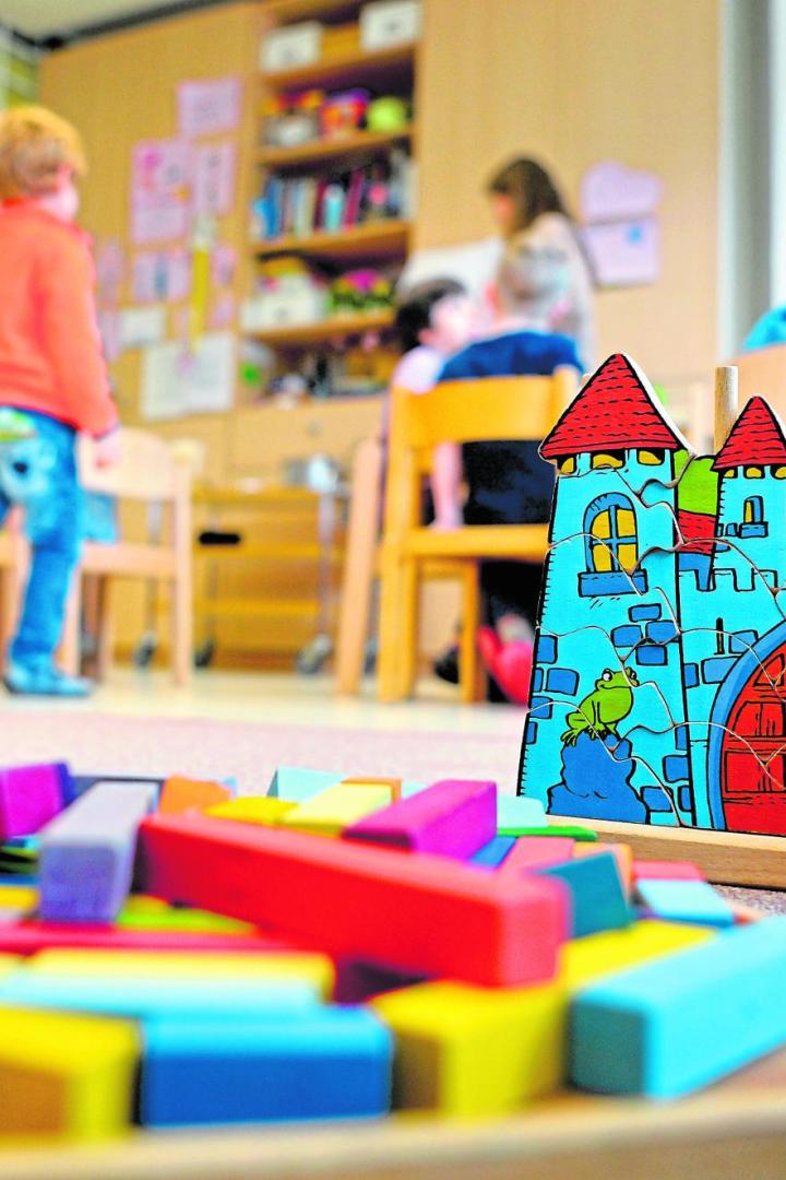 Kinder spielen in einer Kindertagesstätte mit einem Holzpuzzle und Bauklötzen.