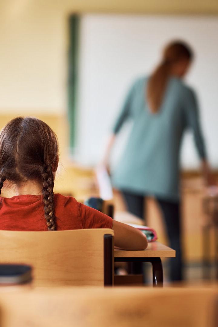 Eine Schulklasse mit einer Lehrerin vor der Tafel und Schülern an ihren Tischen.