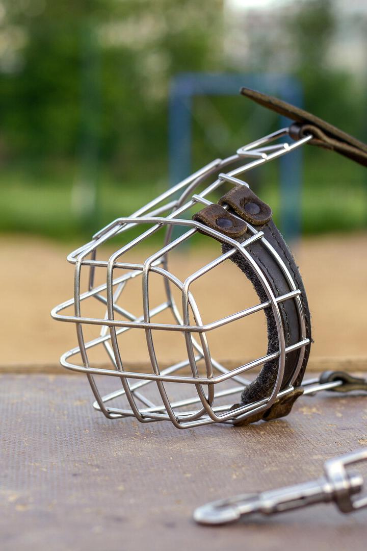 Auf einem Tisch liegt ein Hundemaulkorb mit Metallgitter und Lederriemen im Freien.
