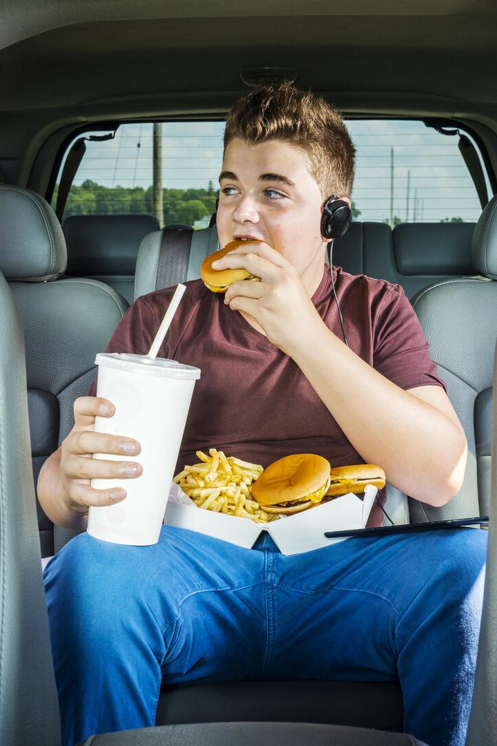 Ein Teenager im Auto isst Burger und Pommes.