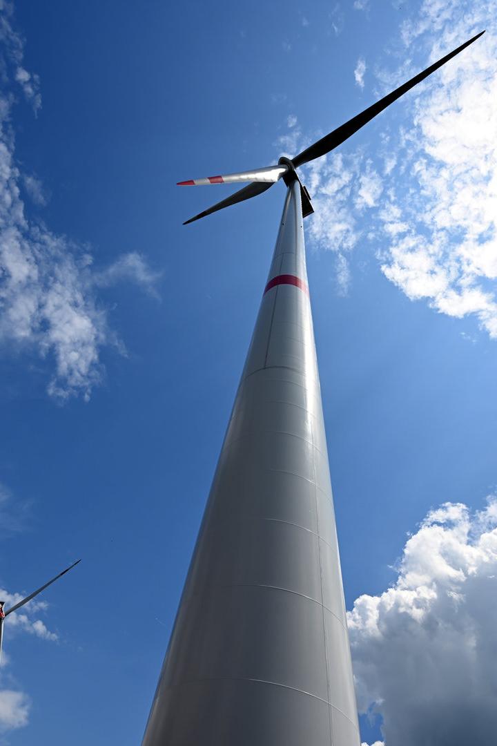 Ein Windrad ragt vor einem Himmel mit weißen Wolken in die Höhe.