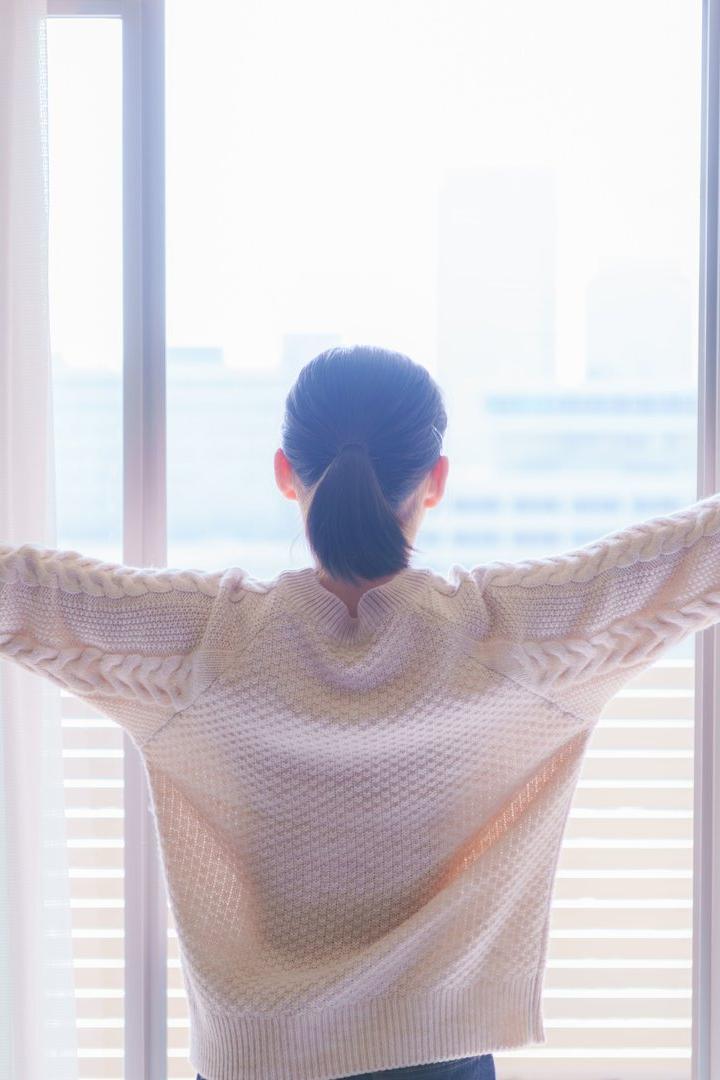 Eine Frau steht am Fenster und lüftet den Raum.