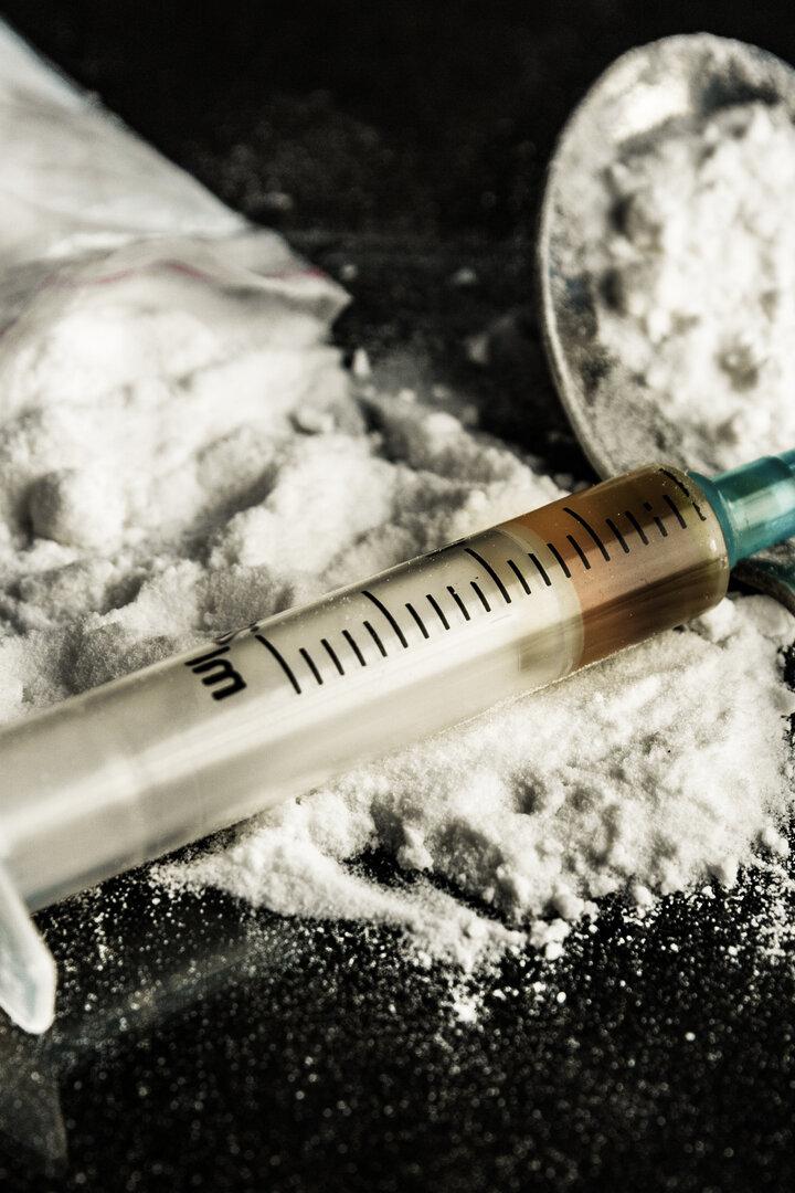 Spritze und Löffel für Drogenkonsum, dahinter Drogen in Pulverform