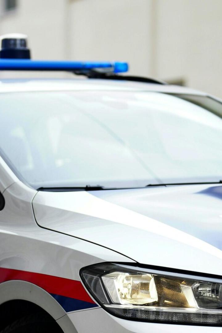 Ein silbernes Polizeiauto mit eingeschaltetem Blaulicht steht auf einer Straße vor einem Gebäude.