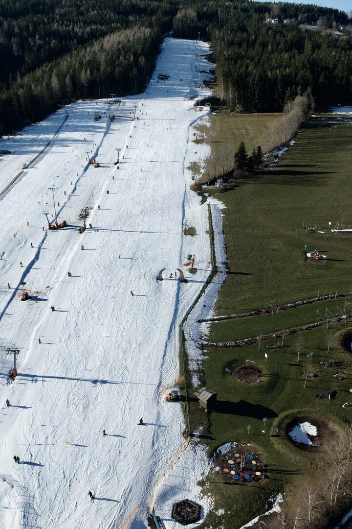 „Wexl-Spiel“ der Jahreszeiten. Links fahren Kinder Ski, rechts daneben wird im Motorikpark geklettert.