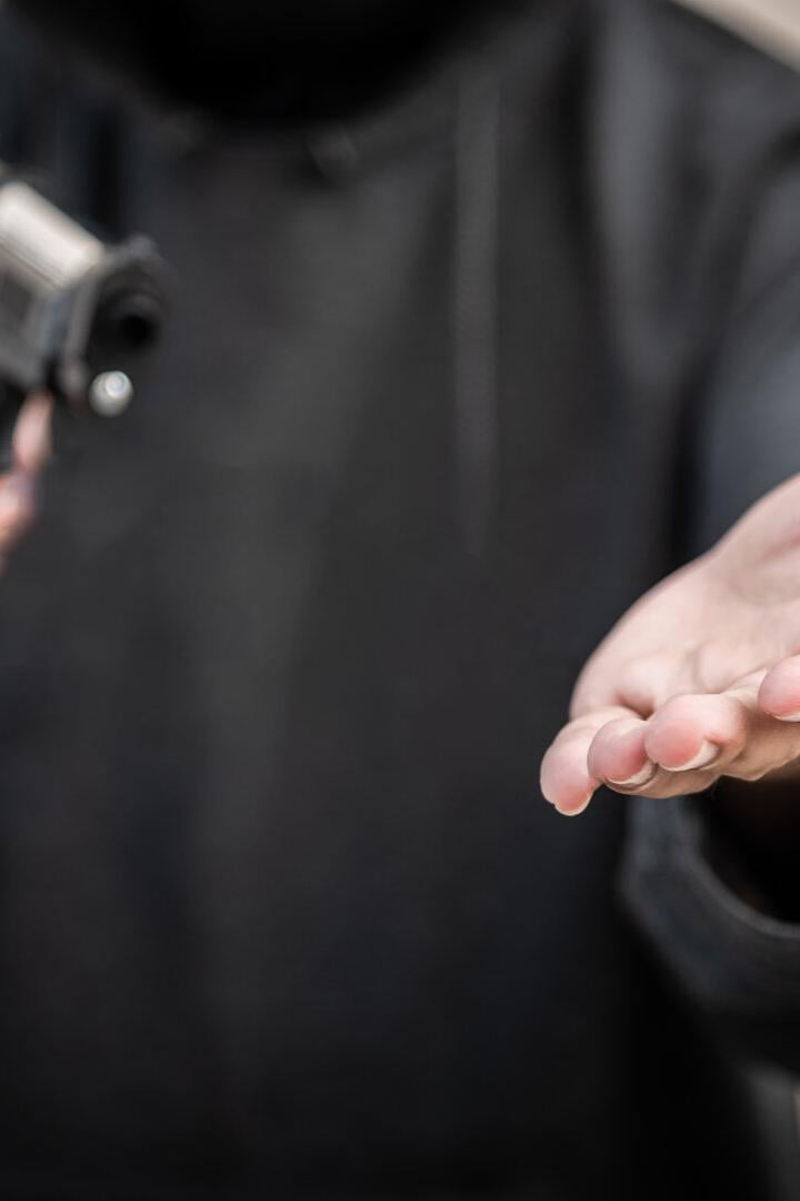 Eine Person in einem schwarzen Hoodie hält eine Pistole in der einen und eine offene Hand in der anderen.