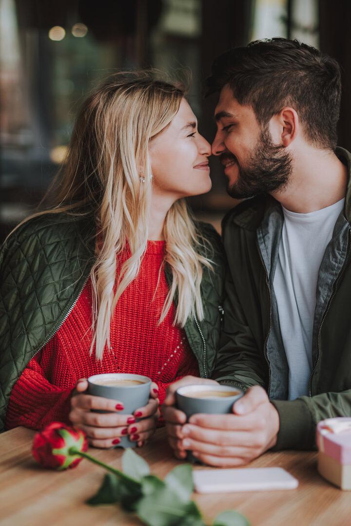 Ein verliebtes Paar sitzt in einem Café und hält Händchen über Tassen.