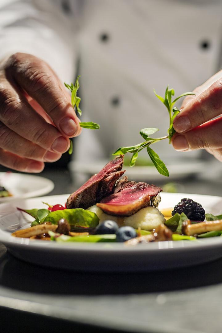 Ein Koch garniert ein Gericht mit Fleisch, Beeren und Gemüse.