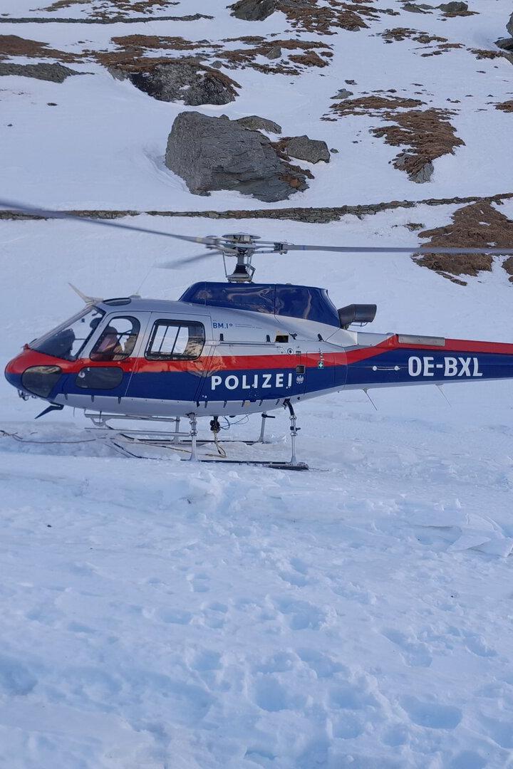 Ein Mann steht neben einem Polizei-Hubschrauber in einer verschneiten Berglandschaft.