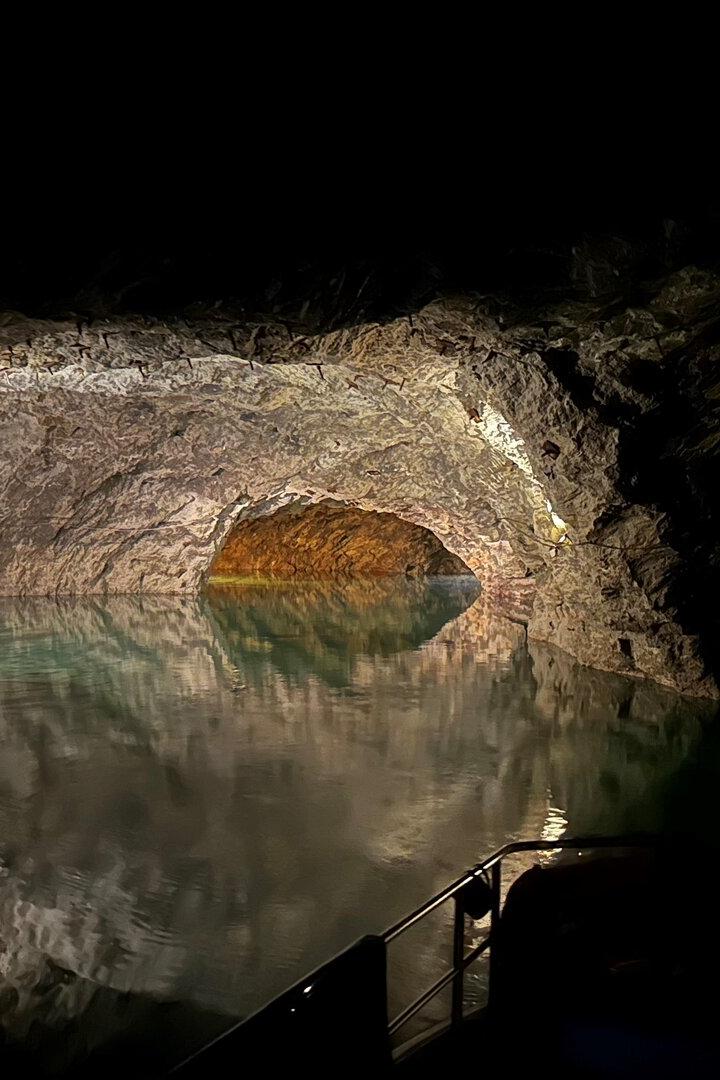 Eine dunkle Grotte mit grünlichem Wasser wird von Felswänden und schwachem Licht umgeben.