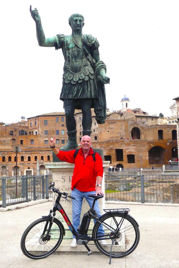 Mann steht mit Fahrrad vor der Caesar-Statue in Rom und macht seine Pose nach