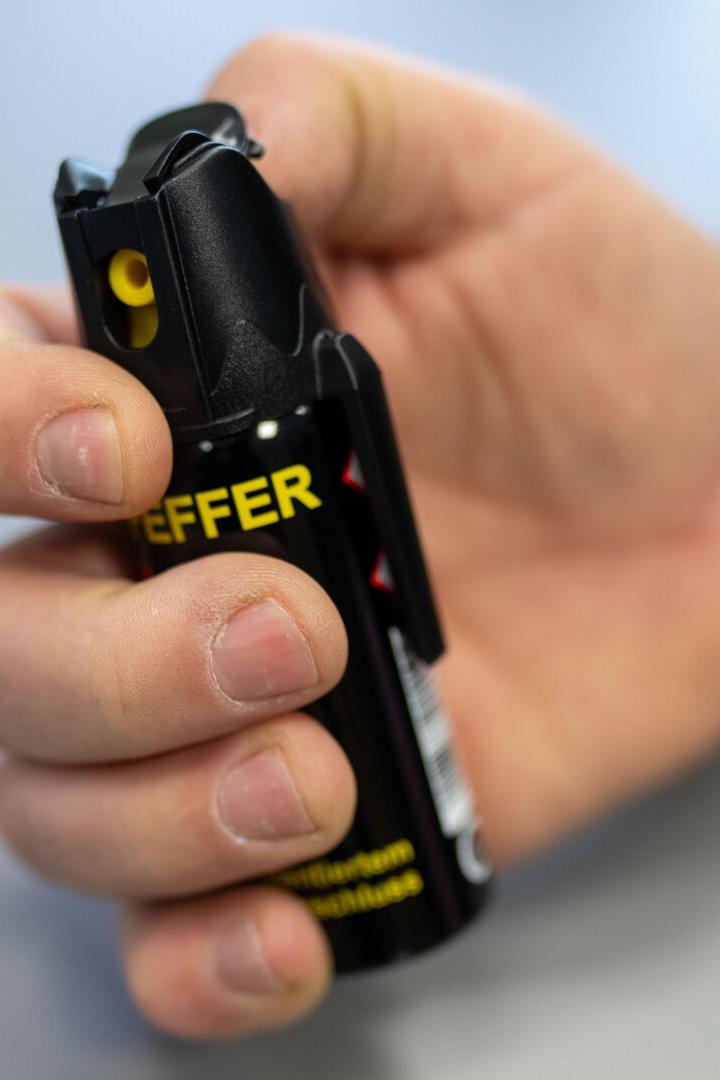Eine Hand hält eine schwarze Pfefferspraydose mit gelber Aufschrift und bereitet sich auf die Benutzung vor.