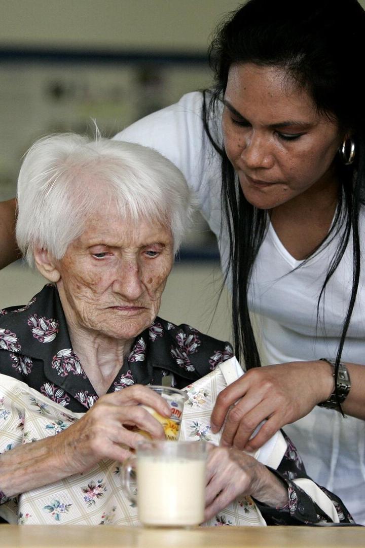 Eine ältere Frau bekommt von einer jüngeren Frau ein Lätzchen umgebunden.