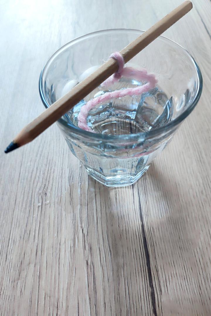 Die Schnur in der Mitte des Stifts befestigen und diesen auf das Glas legen: Das Fadenstück sollte bis zum Glasboden reichen.