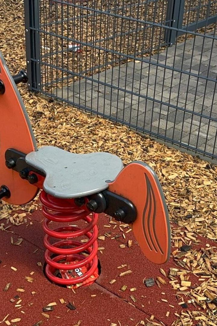 Ein orangefarbenes Schaukeltier in Pferdeform auf einem Spielplatz.