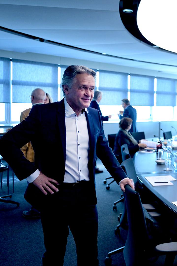 Ein Mann im Anzug, es ist Peter Westenthaler, steht in einem Konferenzraum mit ovalem Tisch und Mikrofonen.