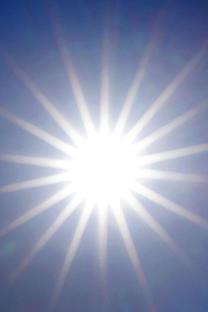Helle Sonne strahlt mit Lichtstrahlen vor blauem Himmel.