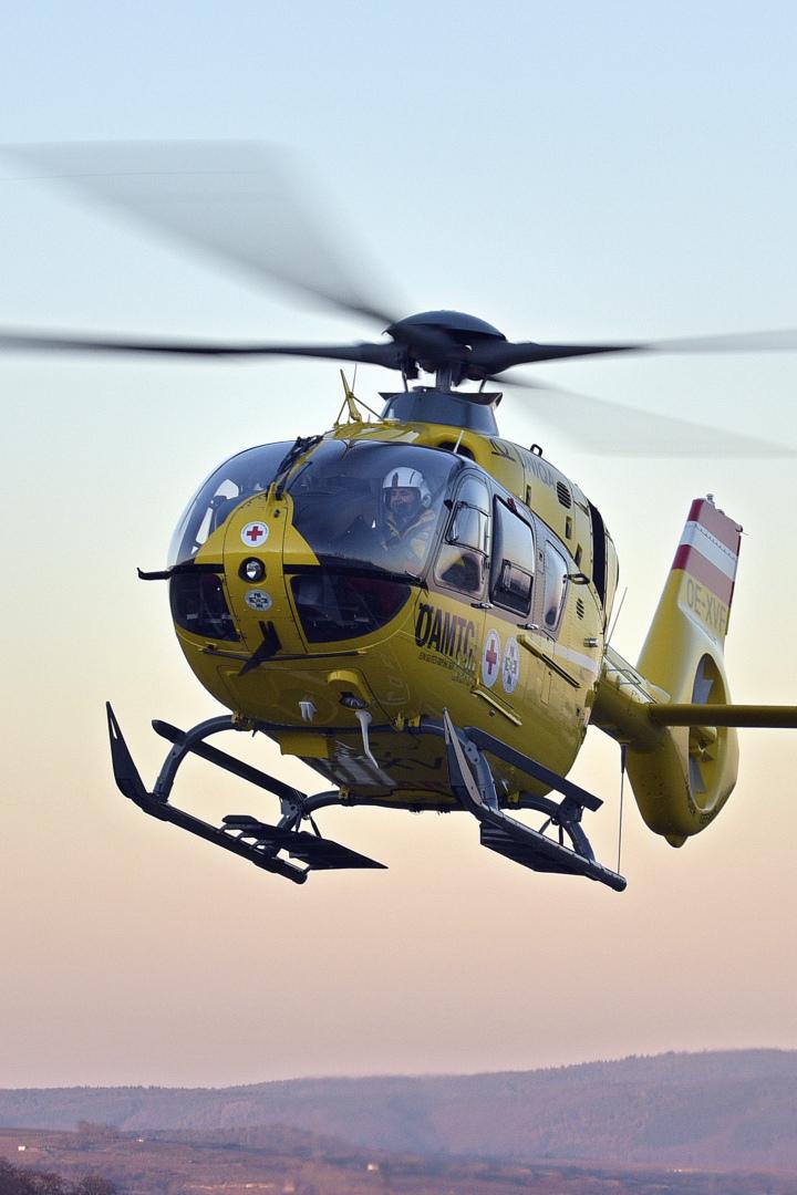 Ein gelber Rettungshubschrauber fliegt knapp über einer hügeligen Landschaft bei klarem Himmel.