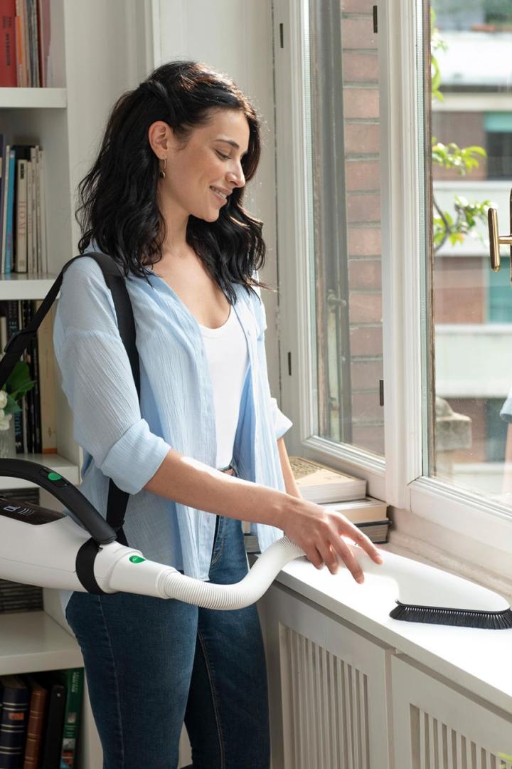 Eine Frau reinigt mit einem tragbaren Staubsauger ein Fensterbrett.