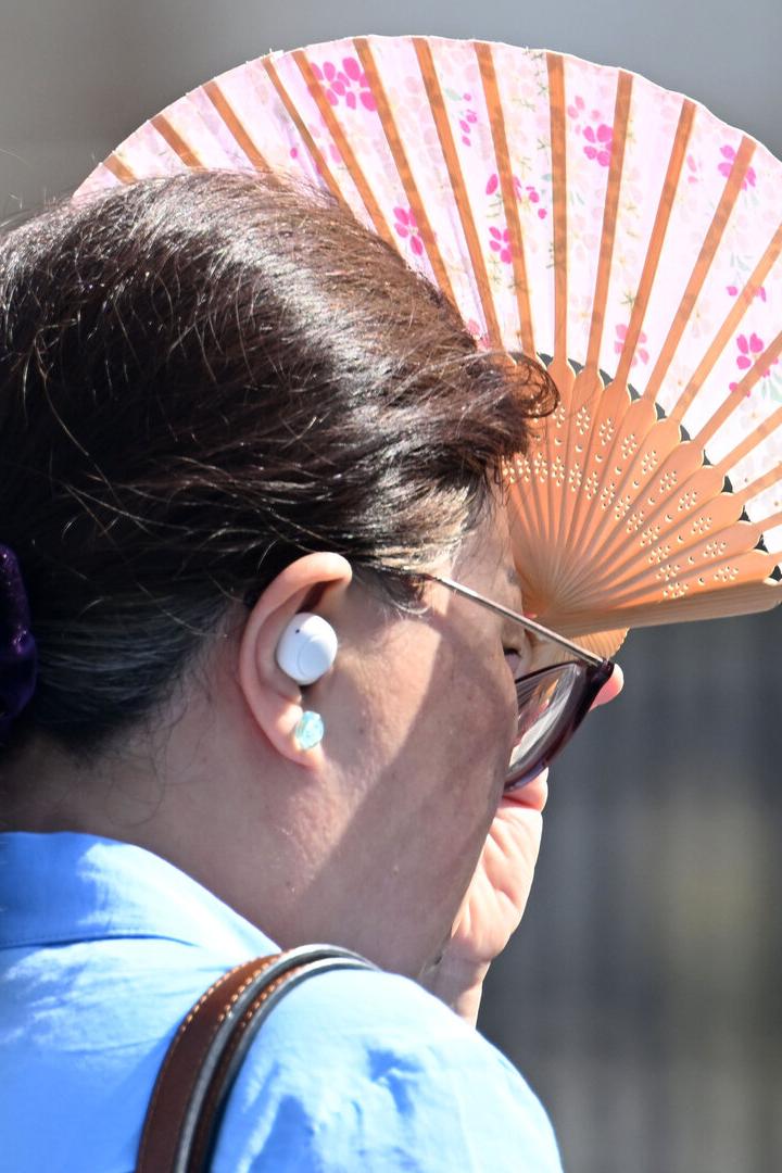 Sommerliche Hitze: Eine Frau schützt sich mit einem Fächer vor der Sonne.