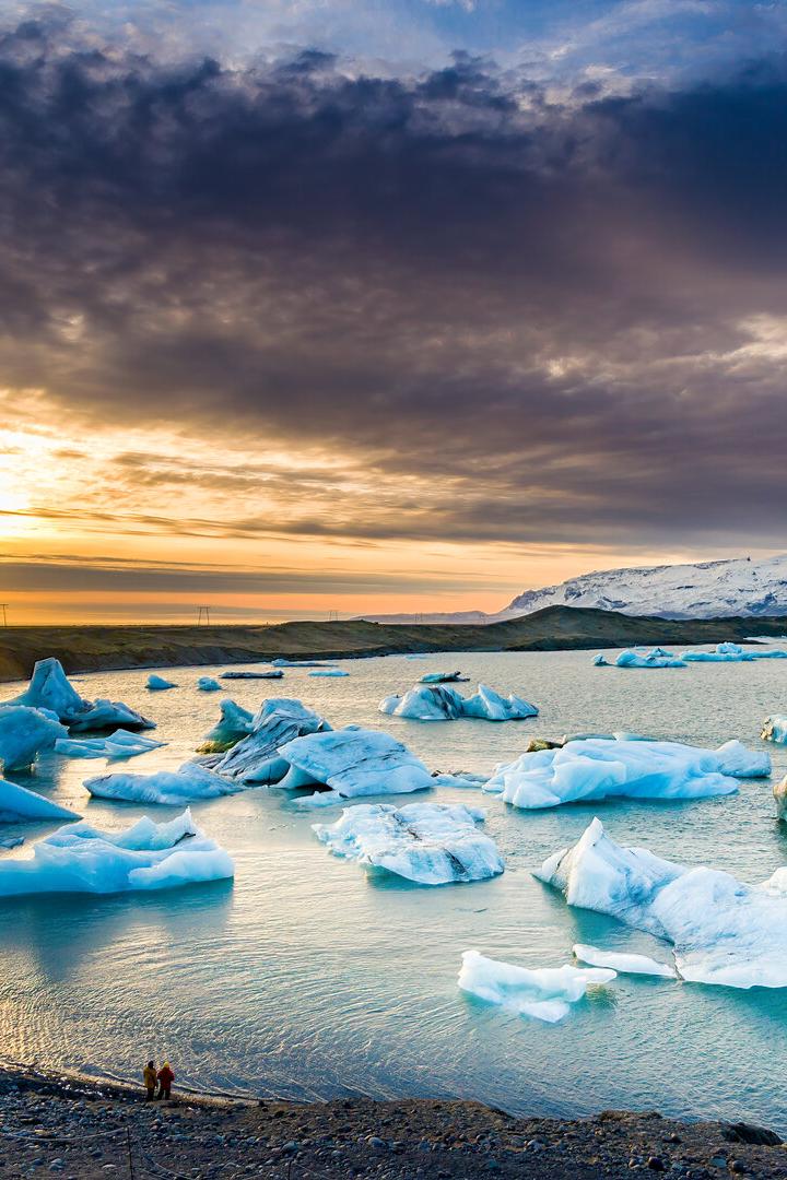 Menschen schauen auf Eisberge in einer Gletscherlagune auf Island bei Sonnenuntergang