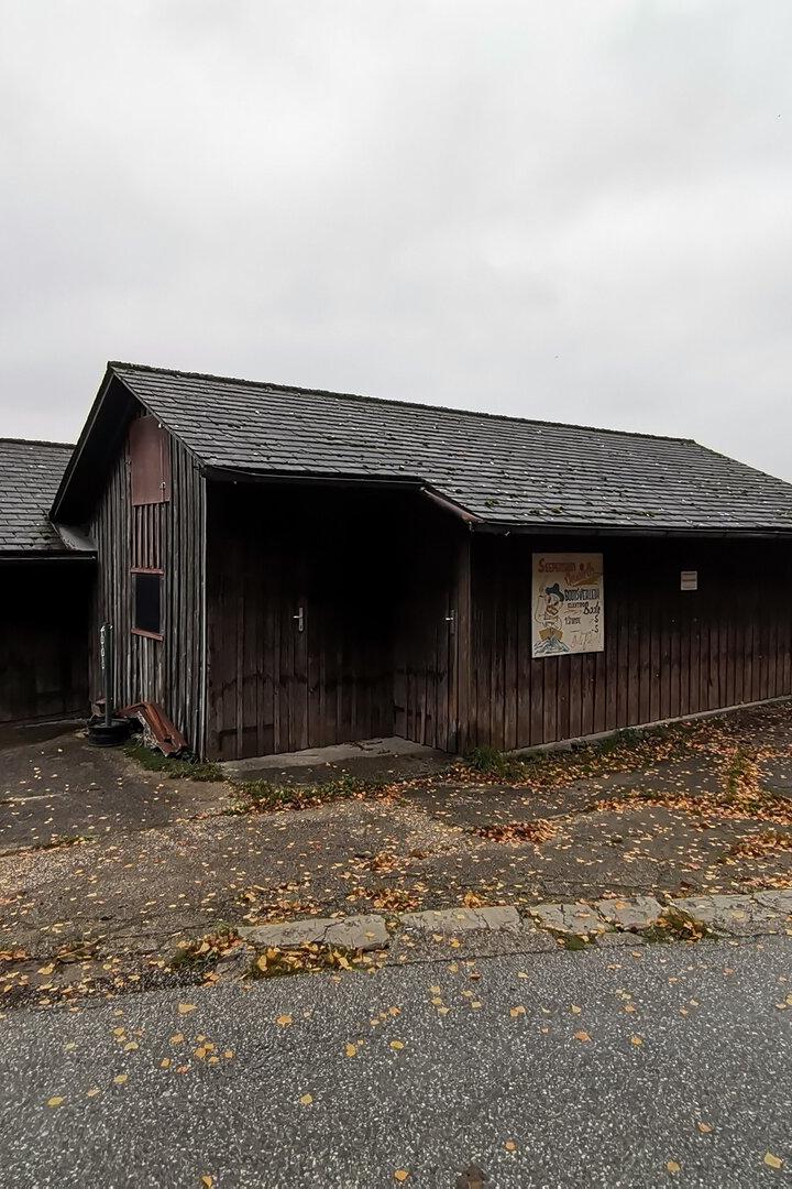Ein kleines, dunkles Holzhaus steht am Ufer eines Sees.