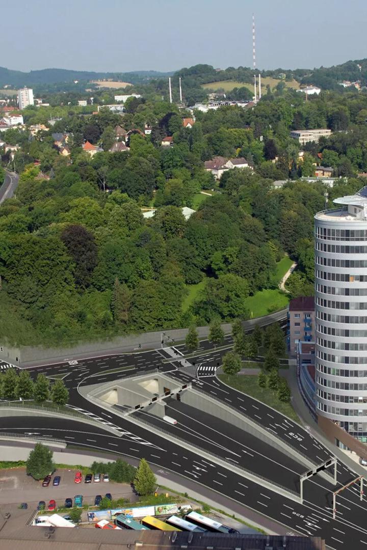 Luftaufnahme einer Stadtlandschaft mit einem modernen Bürogebäude und einer Autobahn mit Tunneln.