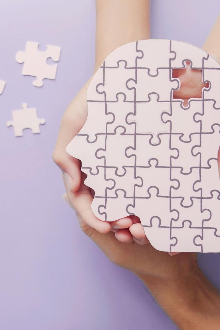 Hände halten ein Puzzle in Form eines Gesichts, bei dem sich einzelne Steine im Bereich des Gehirns lösen. 