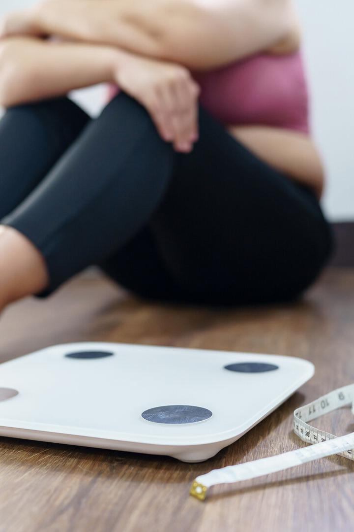 Eine Frau sitzt am Boden neben einer Waage.