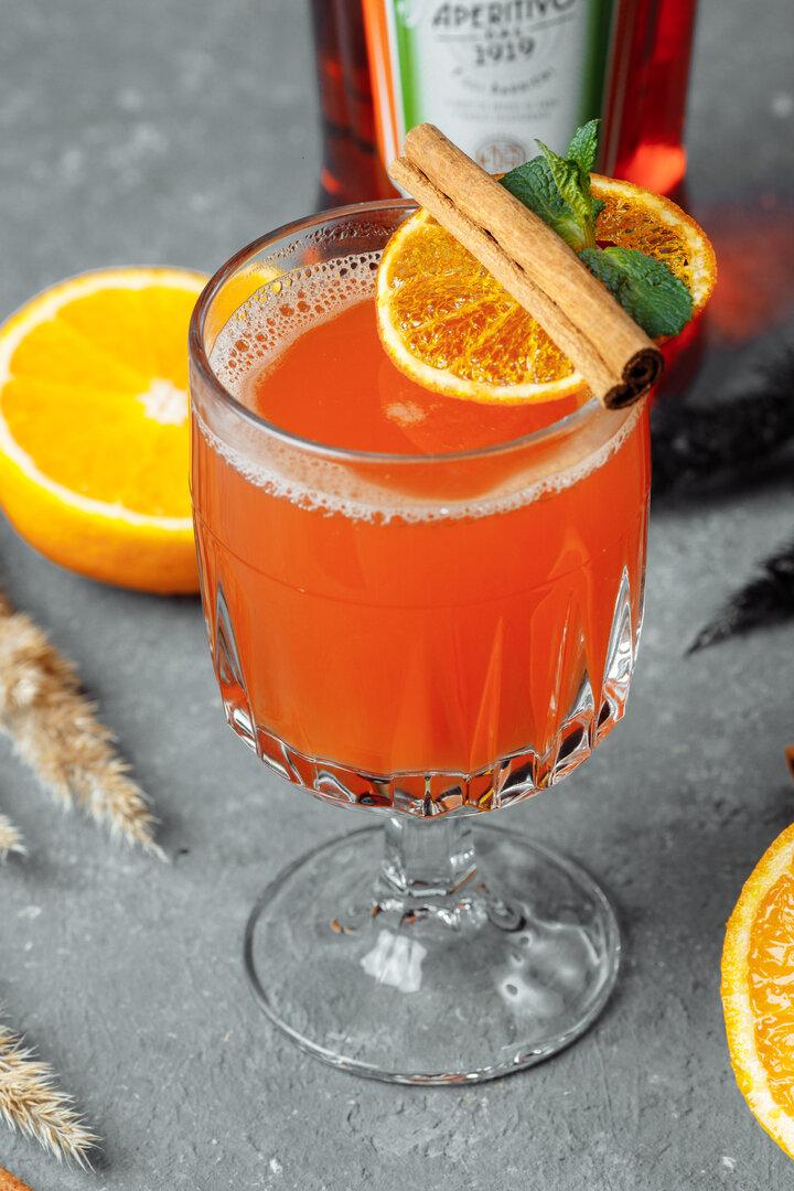 Ein Glas mit einem orangefarbenen Getränk, garniert mit Orange, Zimtstange und Minze.