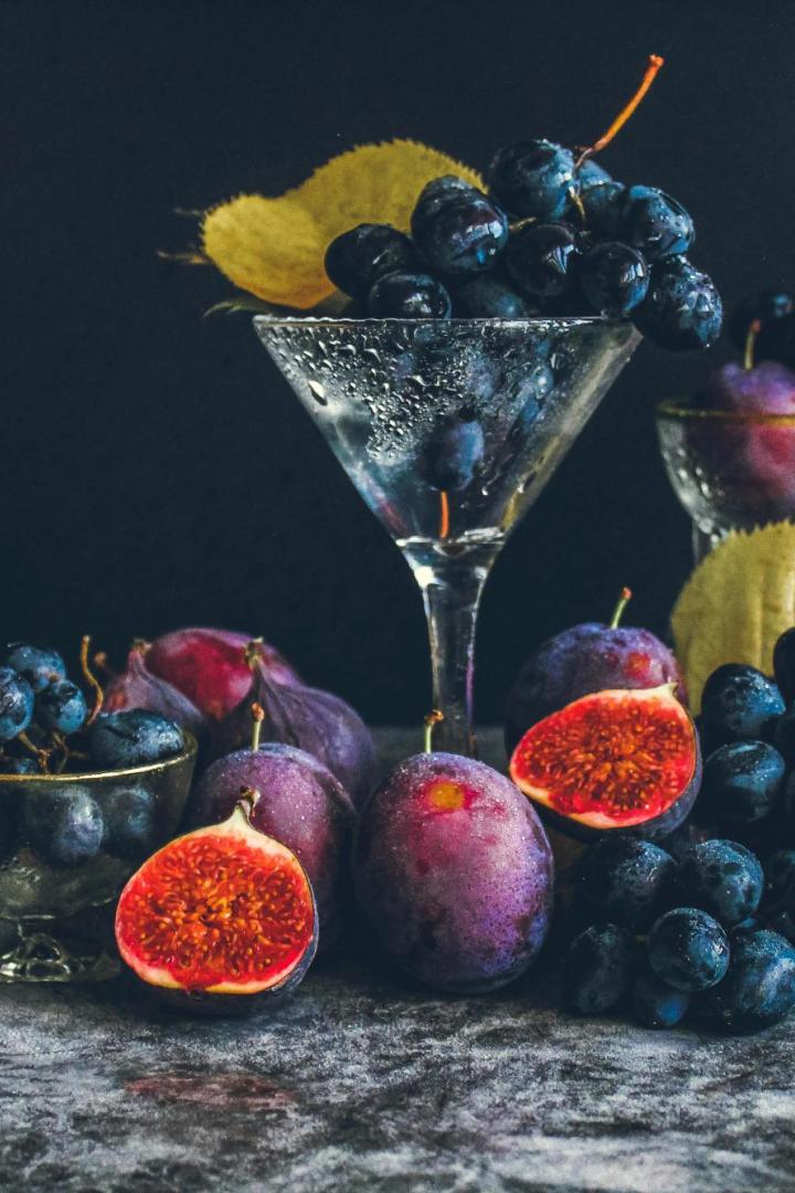 Verschiedene dunkle Trauben, Pflaumen und aufgeschnittene Feigen liegen zusammen mit Blättern auf einer Steinplatte.