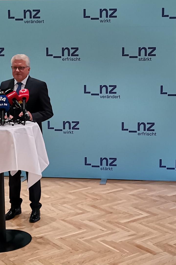 Ein Mann steht vor Mikrofonen bei einer Pressekonferenz, die per Smartphone gefilmt wird.