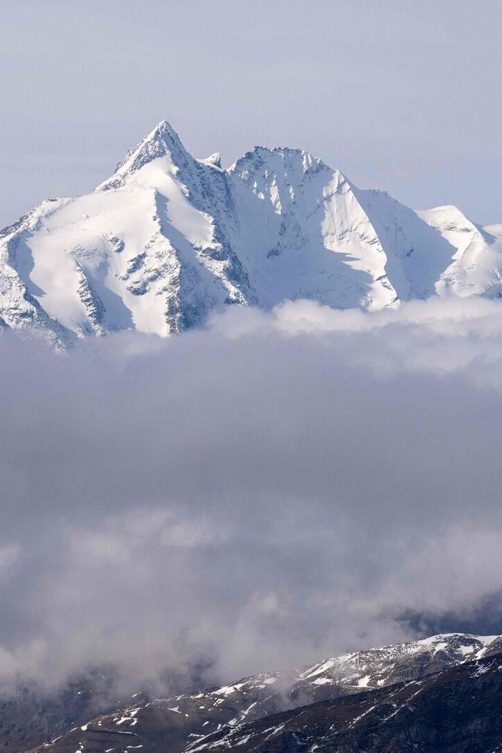 Eine schneebedeckte Bergkette ragt über eine dichte Wolkendecke hinaus.