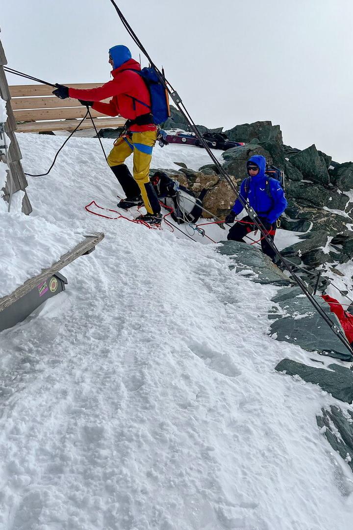 Drei Bergsteiger arbeiten an einem Gebäude in einer verschneiten Berglandschaft.