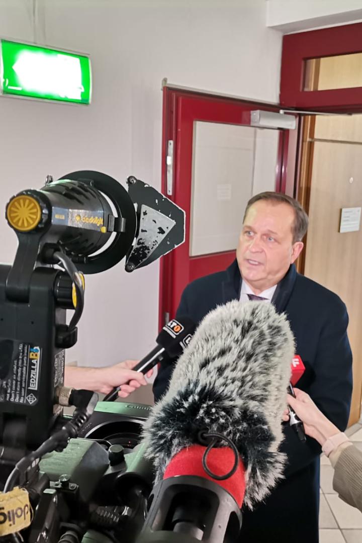 Ein Mann wird von mehreren Reportern mit Mikrofonen interviewt.