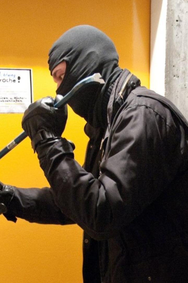 Einbrecher hebelt mit einem Brecheisen eine gelbe Tür auf.