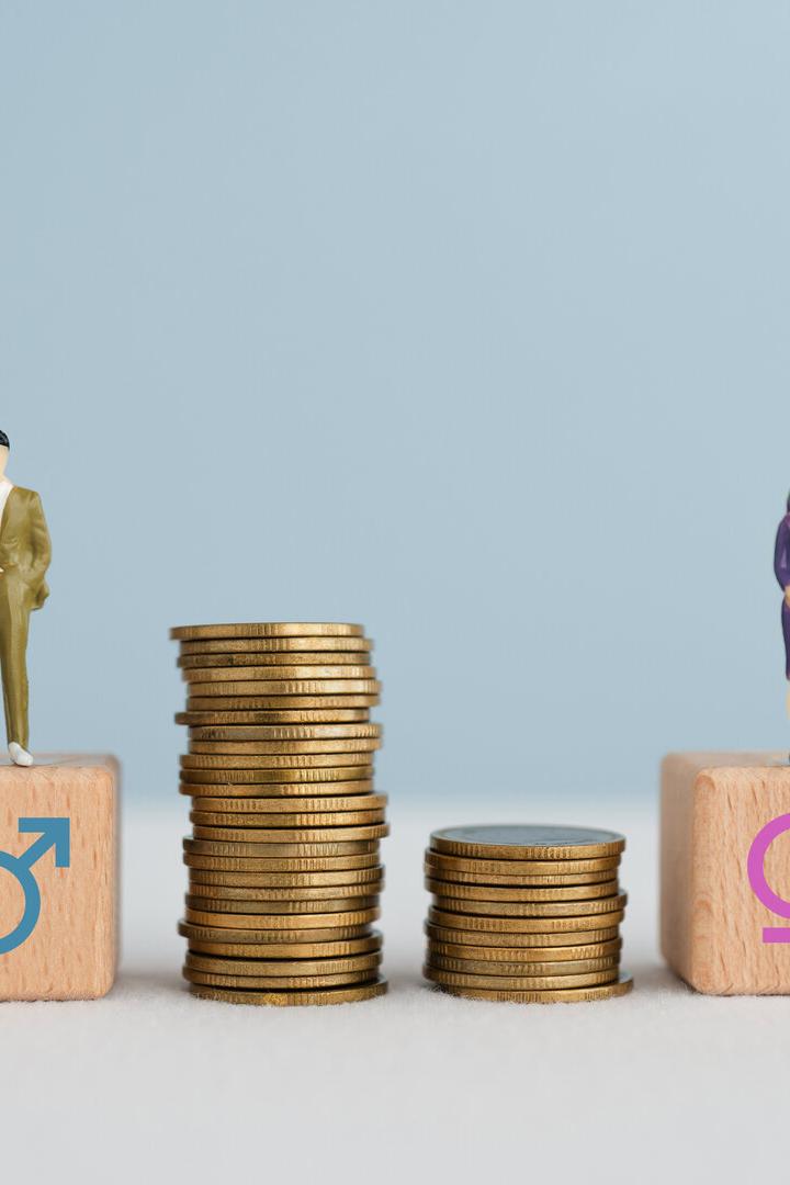 Gender pay equality concept. Miniature of man and woman on wooden cube block with stack of coins