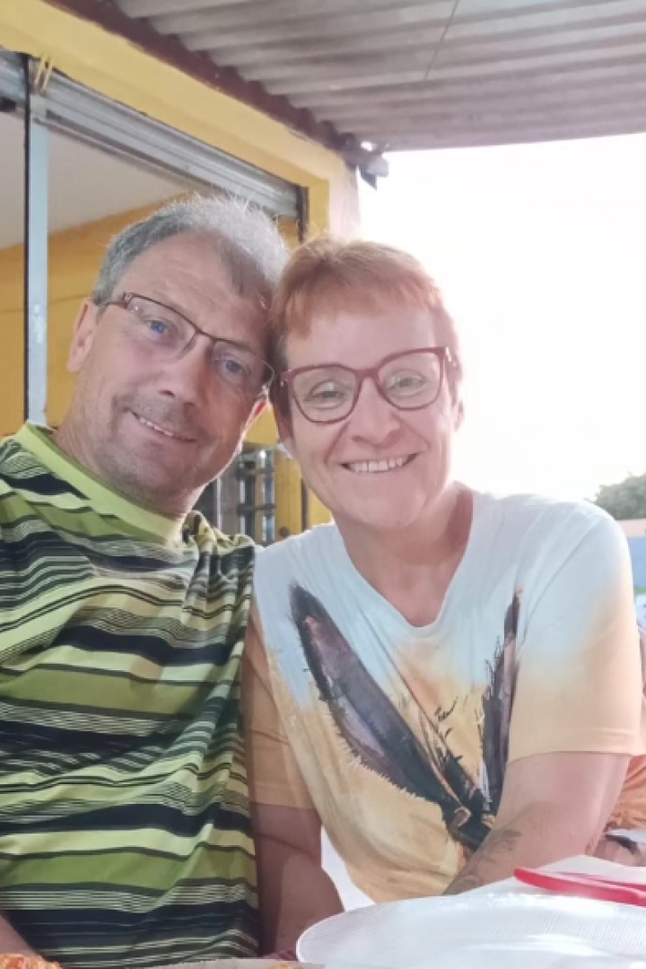Heiko und Ulrike: Ein grauhaariger Mann und eine rothaarige Frau Mitte 50 sitzen lachend nebeneinander