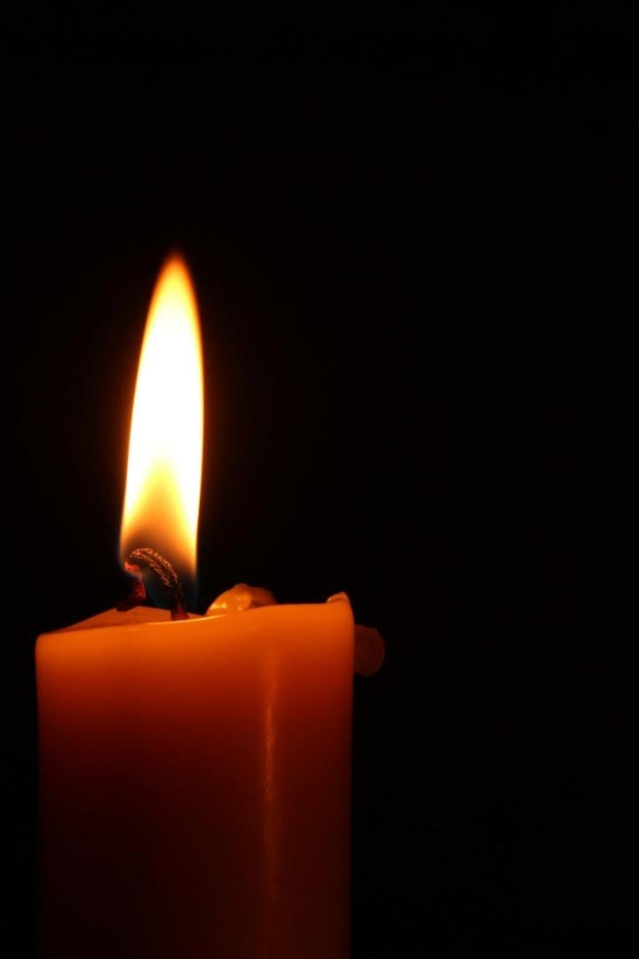 Brennende Kerze vor schwarzem Hintergrund.