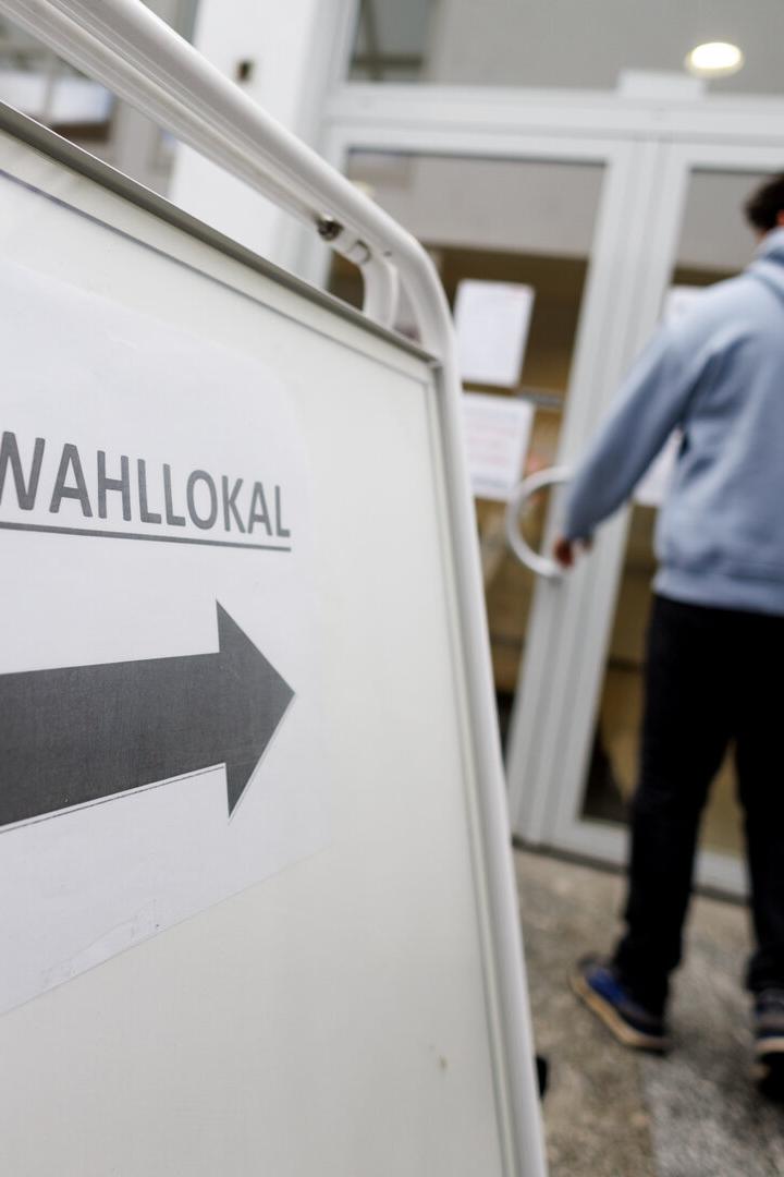 Ein Schild mit der Aufschrift "Zum Wahllokal" und einem Pfeil zeigt die Richtung, während eine Person eintritt.