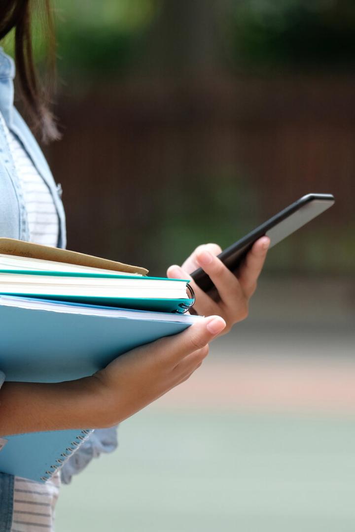 Student girl holding books and smartphone while walking in school campus background, education, back to school concept