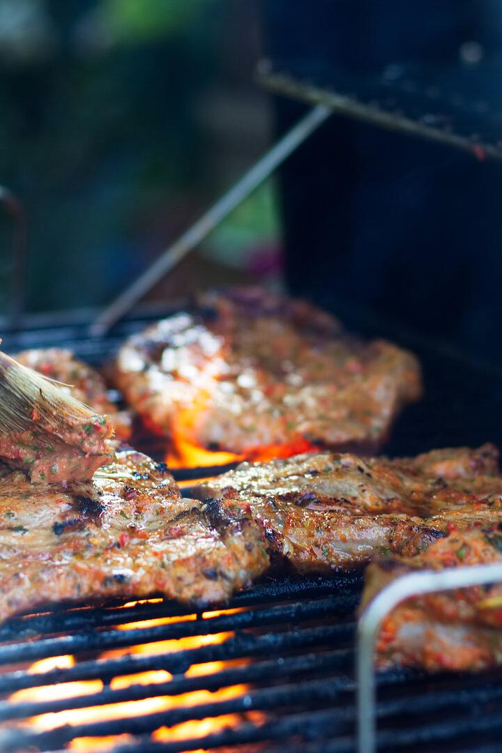 Mit einem Pinsel wird Fleisch auf einem Grill mariniert.
