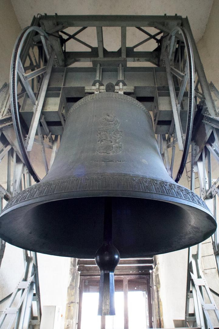 Eine große Glocke hängt in einem metallenen Glockenstuhl vor einem hellen Fenster.