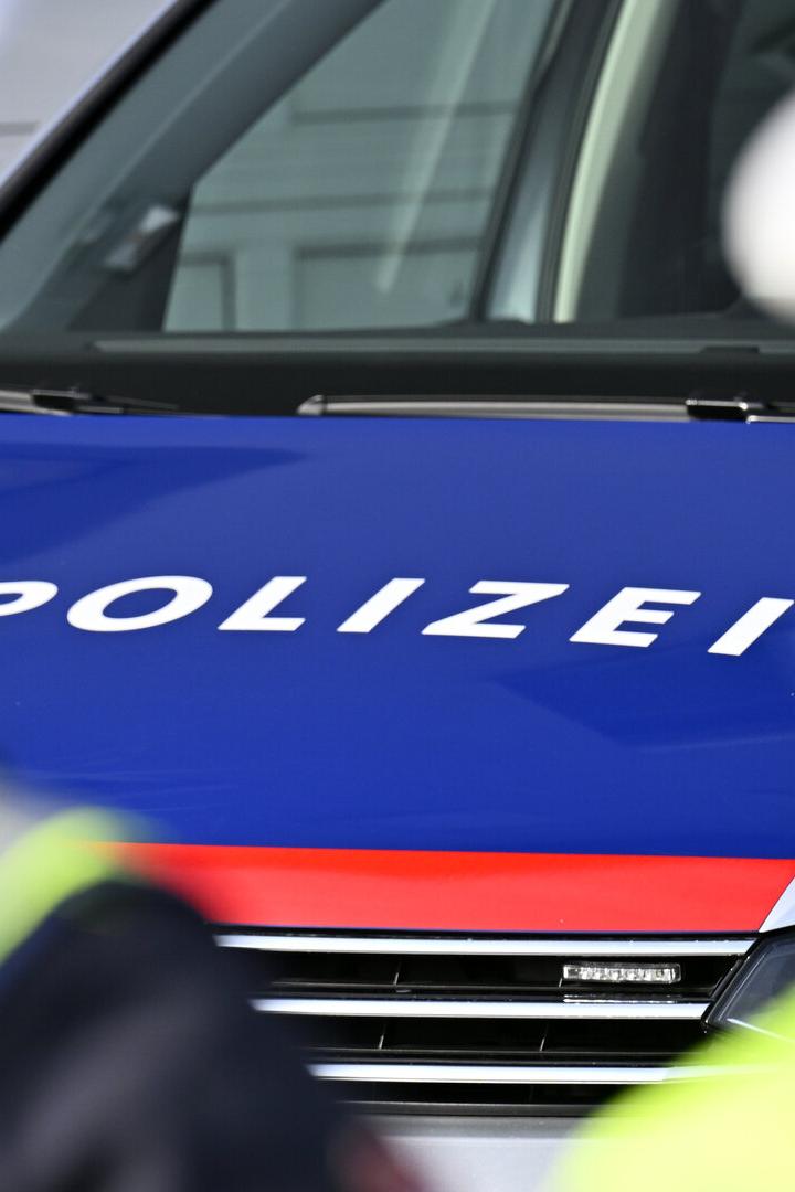 Zwei Polizisten in Warnwesten stehen vor einem Polizeiauto mit blau-roter Motorhaube und dem Schriftzug „Polizei“.
