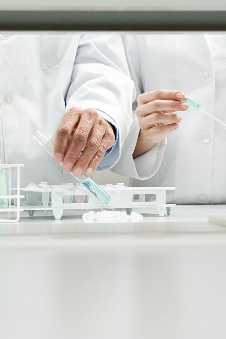 Zwei Personen in Laborkitteln führen Experimente mit Flüssigkeiten und Reagenzgläsern durch.