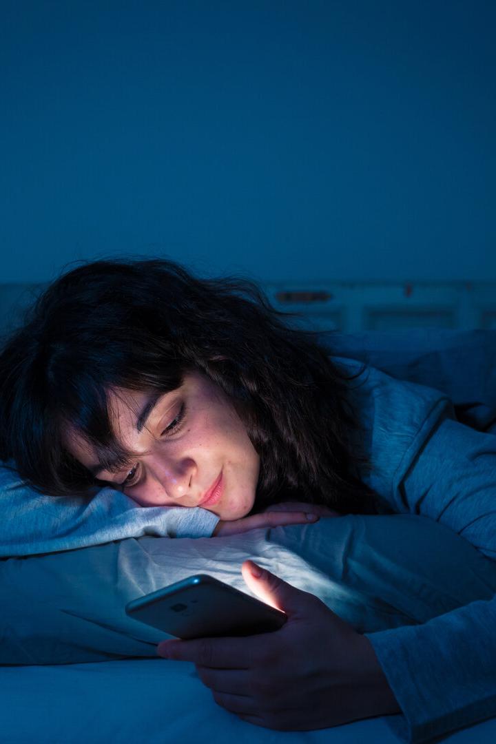 Frau in blauem Licht im Bett mit Handy 