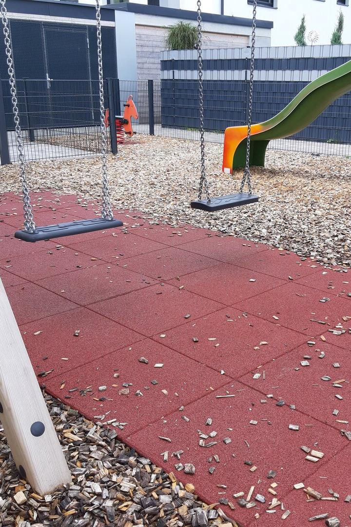 Ein Spielplatz mit Schaukeln, einer Rutsche und einem roten Gummiboden.
