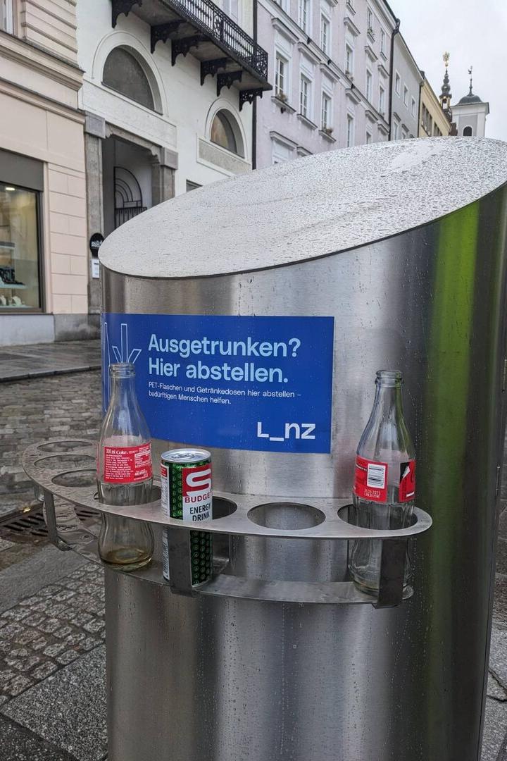 Ein Pfandring mit leeren Flaschen und einer Dose in einer städtischen Umgebung.